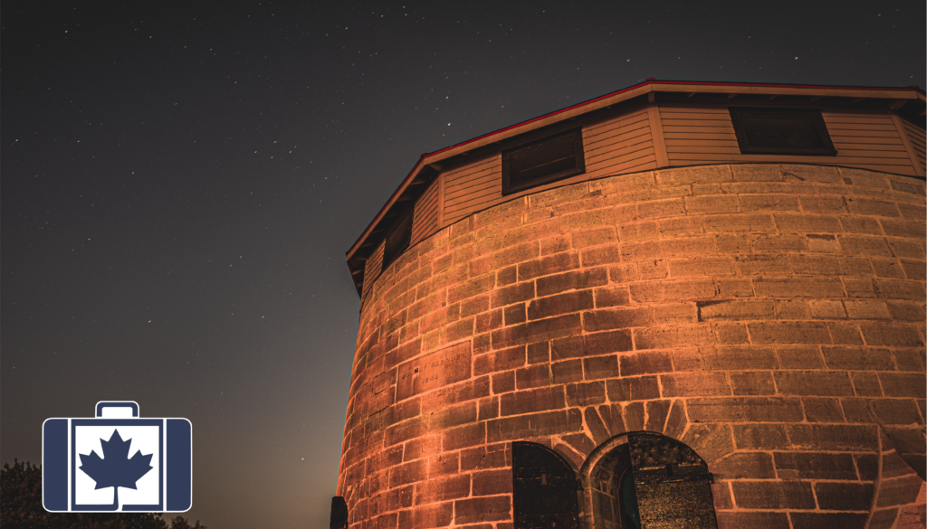 A historic stone Martello tower in Kingston, Ontario, illuminated against a starry night sky.